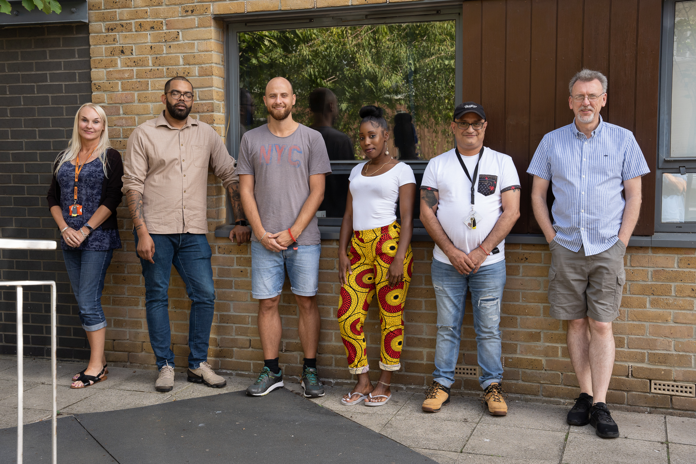 six people standing outside a building in a row smiling at the camera